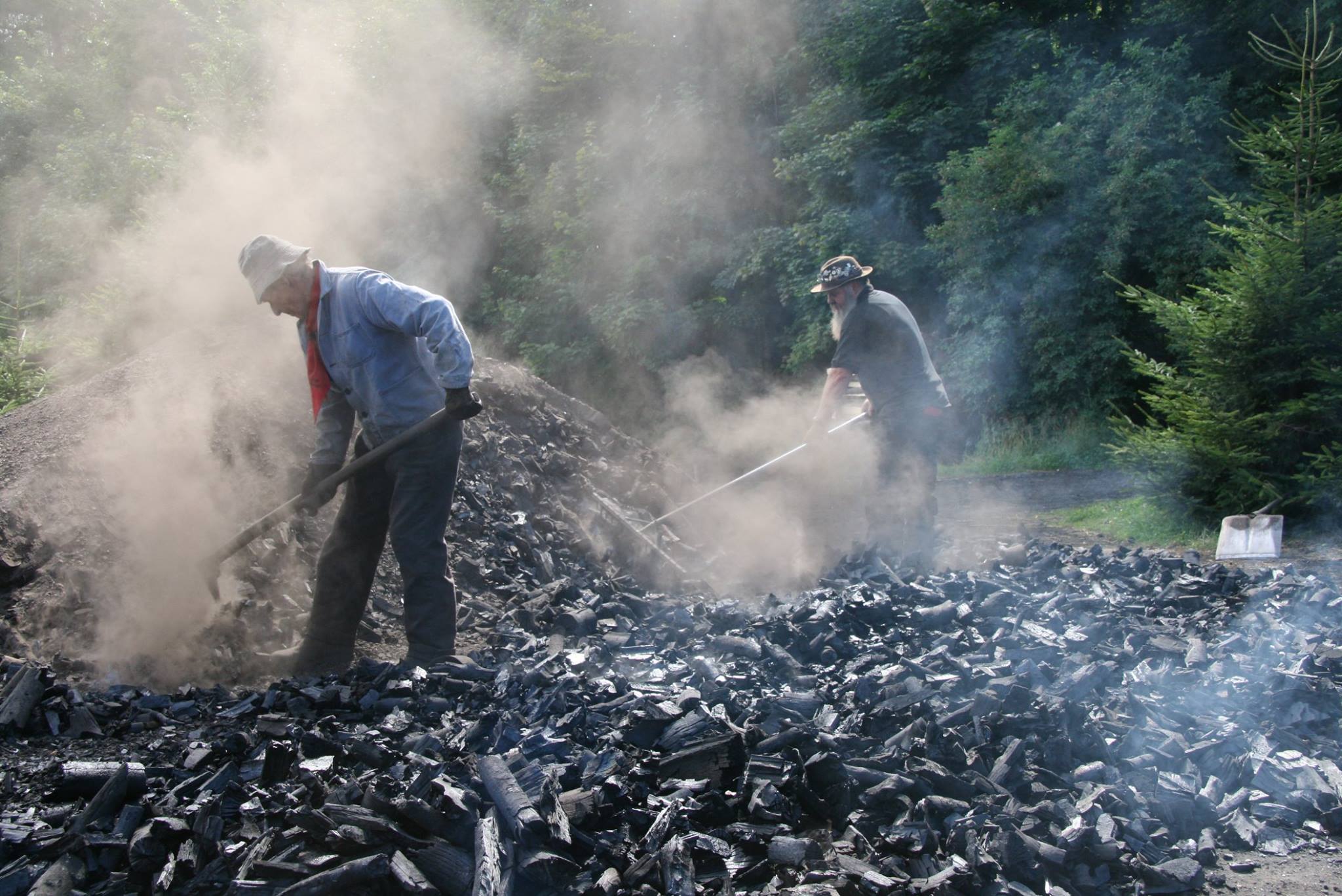 Workers shovel dusty charcoal outdoors