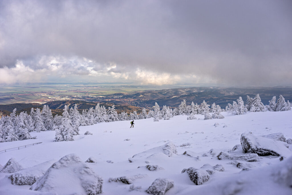 Verschneiter Brocken mit Wanderer. Winterlandschaft mit Blick ins Tal.